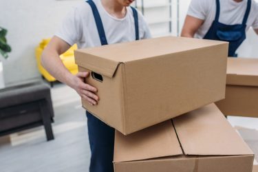 cropped view of two movers transporting cardboard boxes in apartment cropped view of two movers transporting cardboard boxes in apartment
